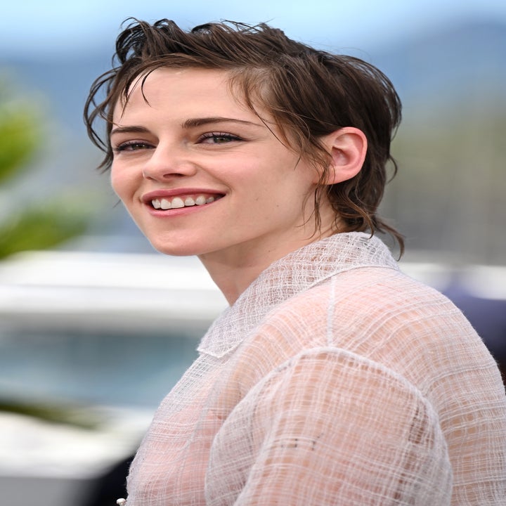 Person with short, styled hair wearing a textured, sheer outfit, smiling at a formal event