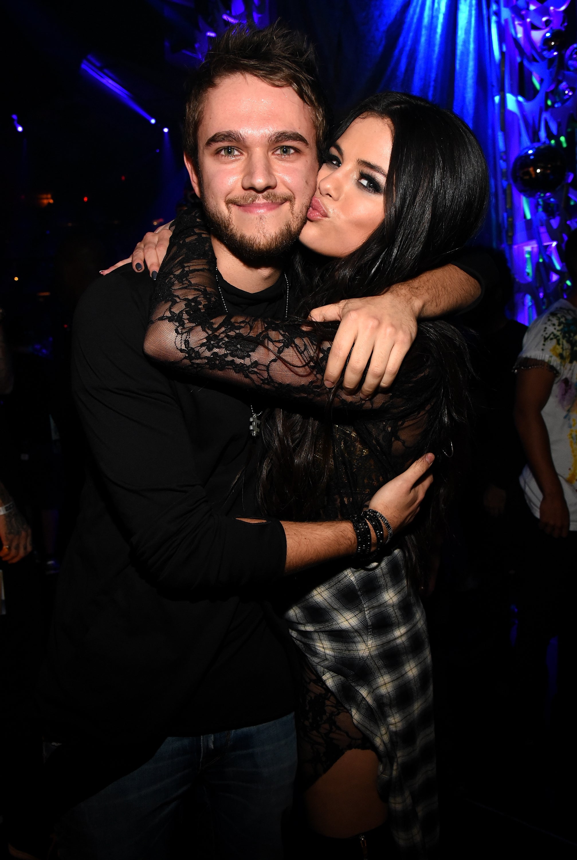 Two people embracing at a celebrity event; one is giving a playful kiss on the cheek. They are dressed in casual evening attire