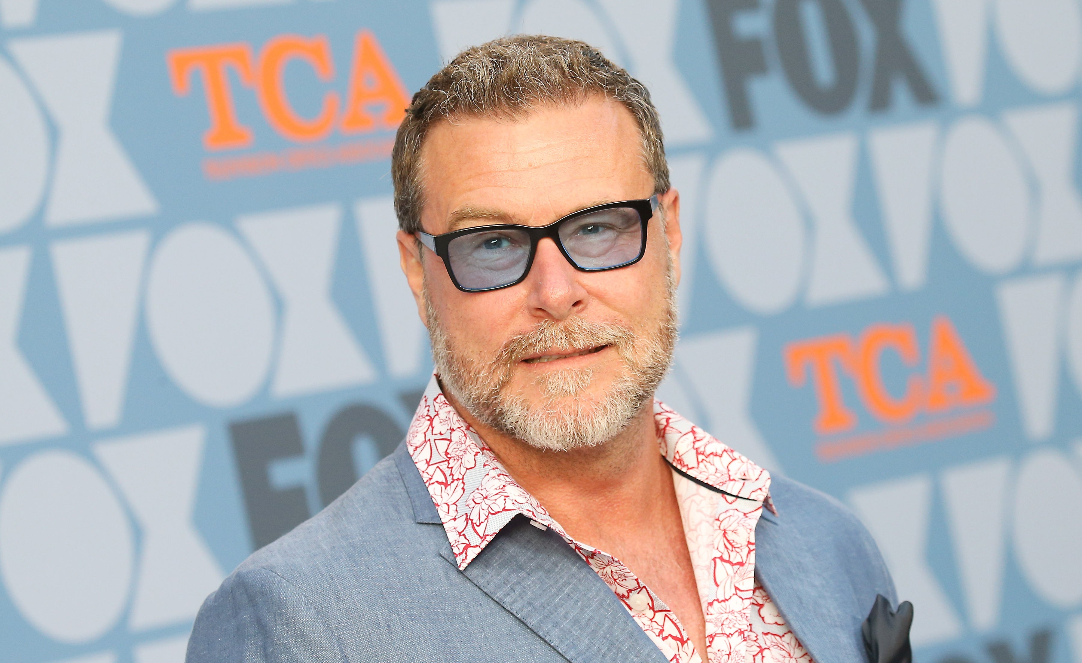 A person in a patterned shirt and suit jacket poses at a FOX event, wearing glasses