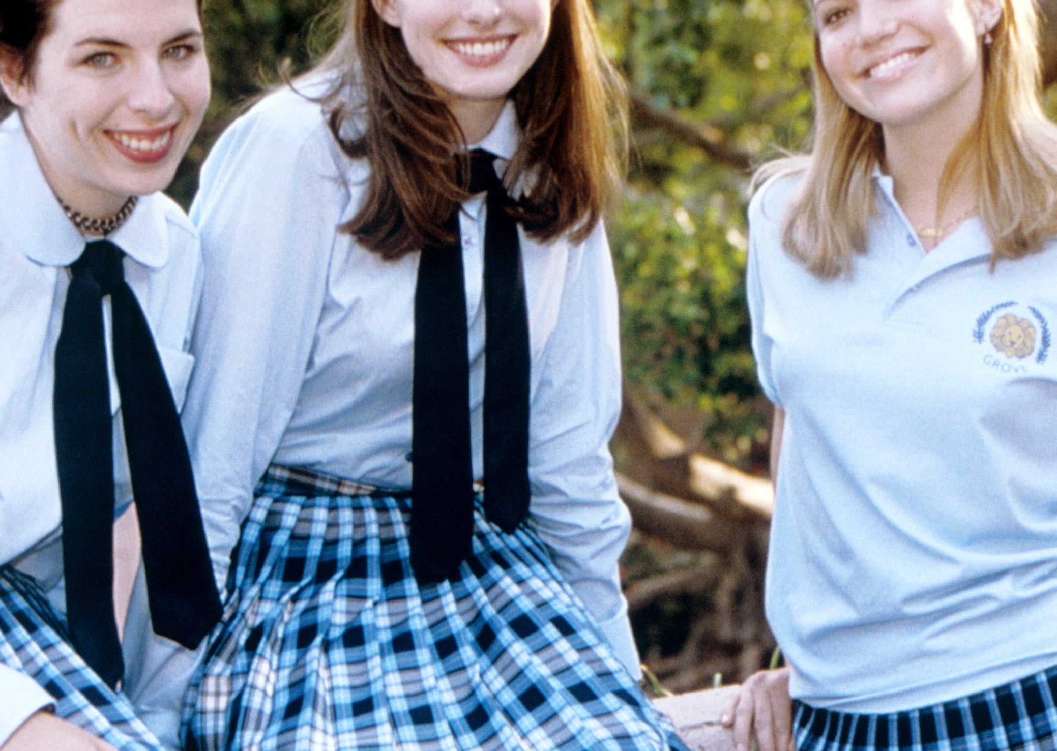 Three people in blue plaid skirts and uniforms, smiling outdoors in a school setting