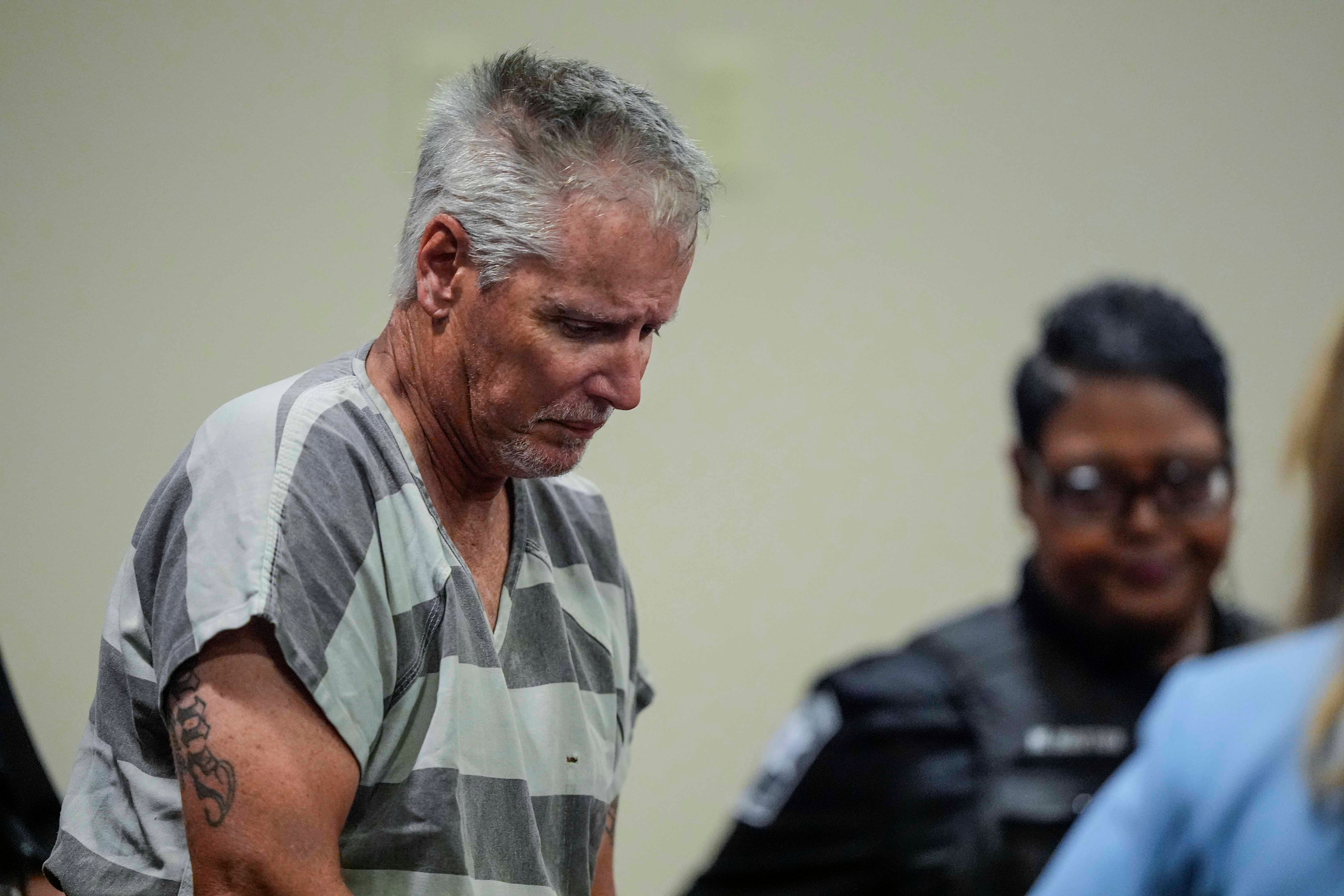 A man in a striped prison jumpsuit appears in court, accompanied by security personnel