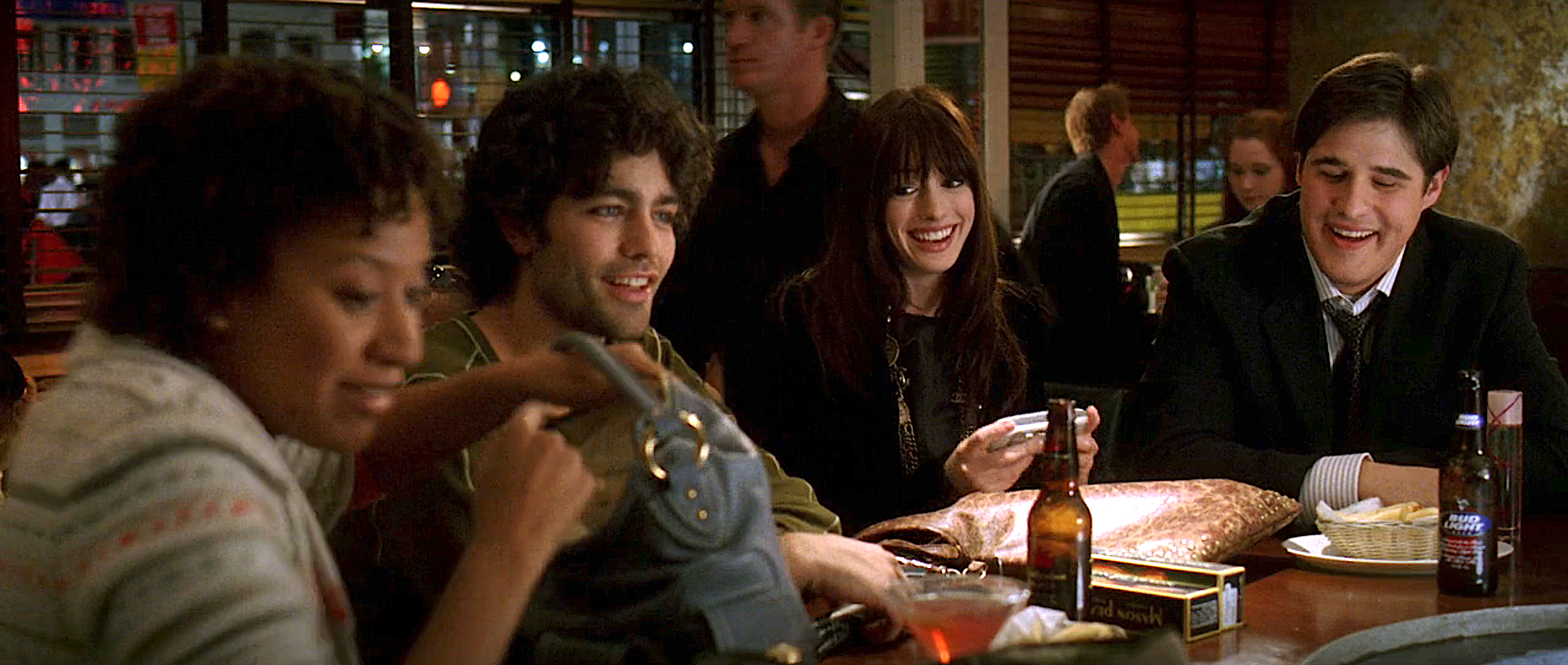 Four people sitting at a bar, chatting and smiling, with drinks and a bag on the counter in front of them