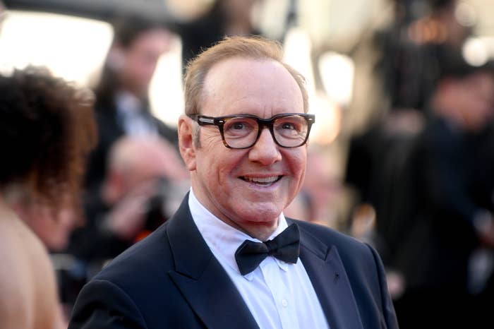 A person in a suit and bow tie on the red carpet, smiling and looking towards the camera