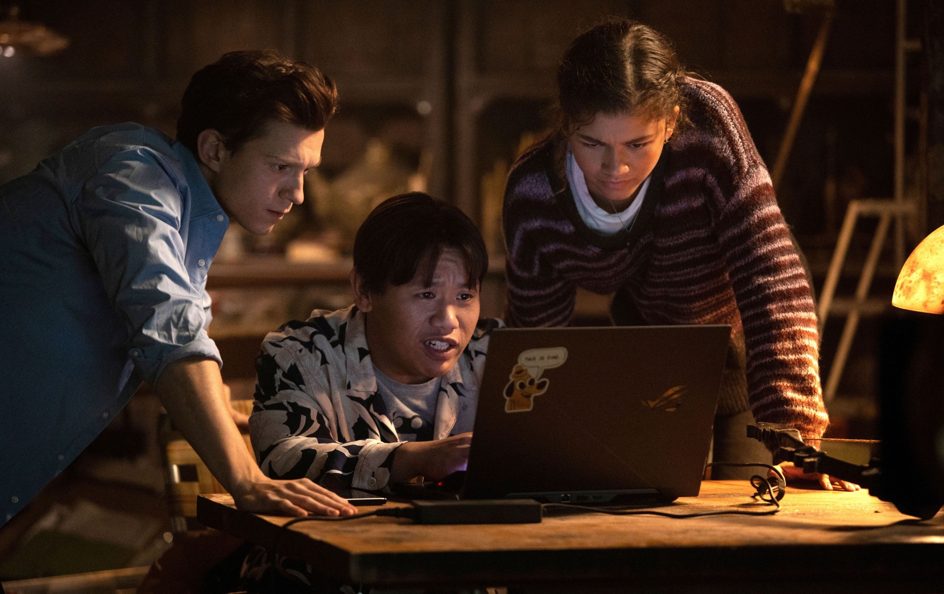 Three people look intently at a laptop screen, appearing focused and engaged in a discussion