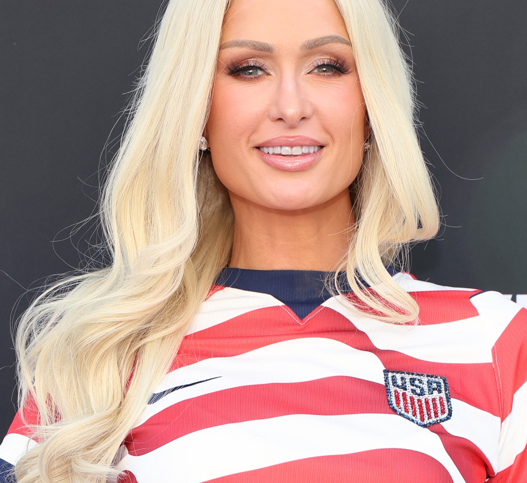 Person in a USA soccer jersey with long, wavy hair, smiling at an event