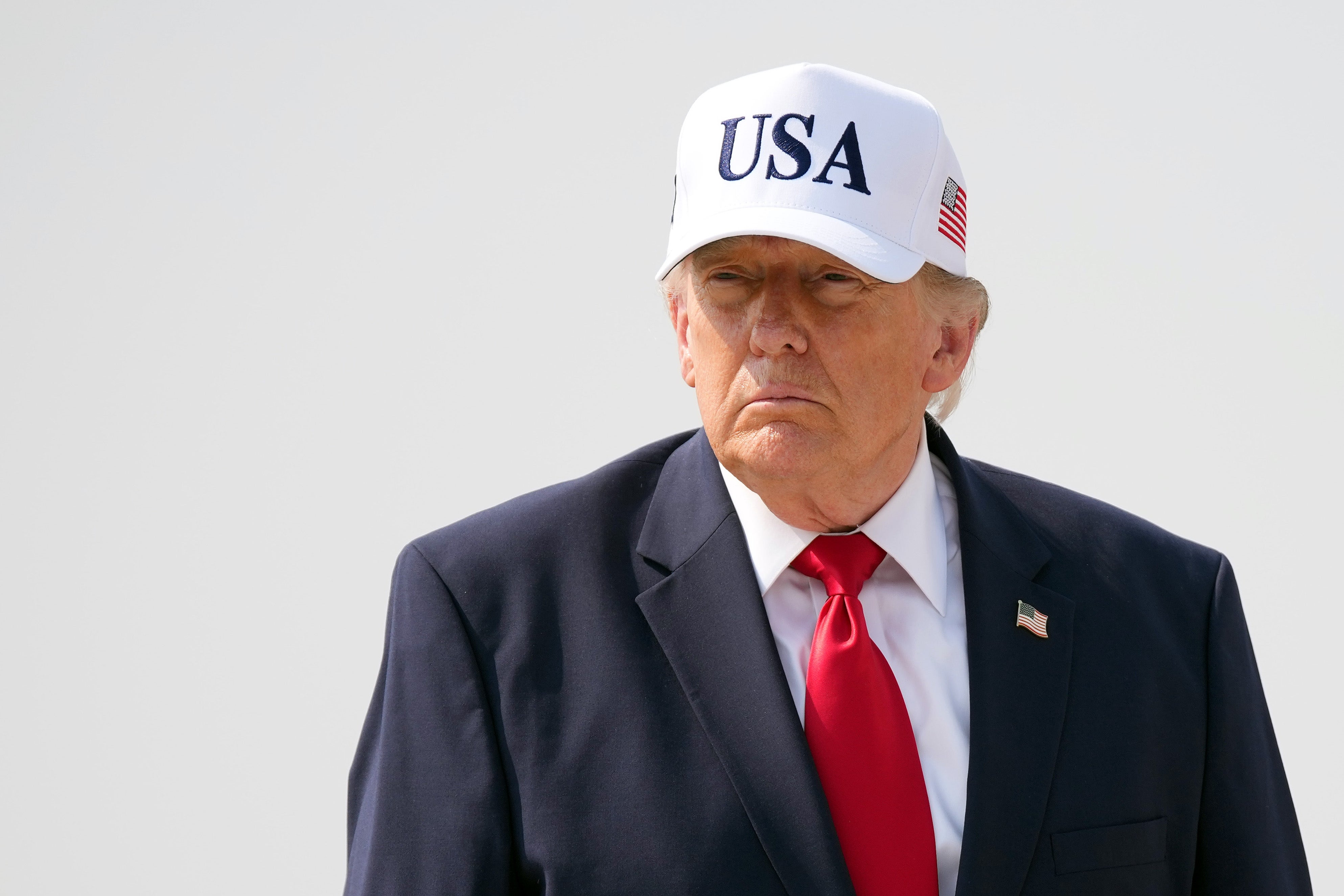 A person in a suit with a red tie and a white cap that says "USA," standing outdoors