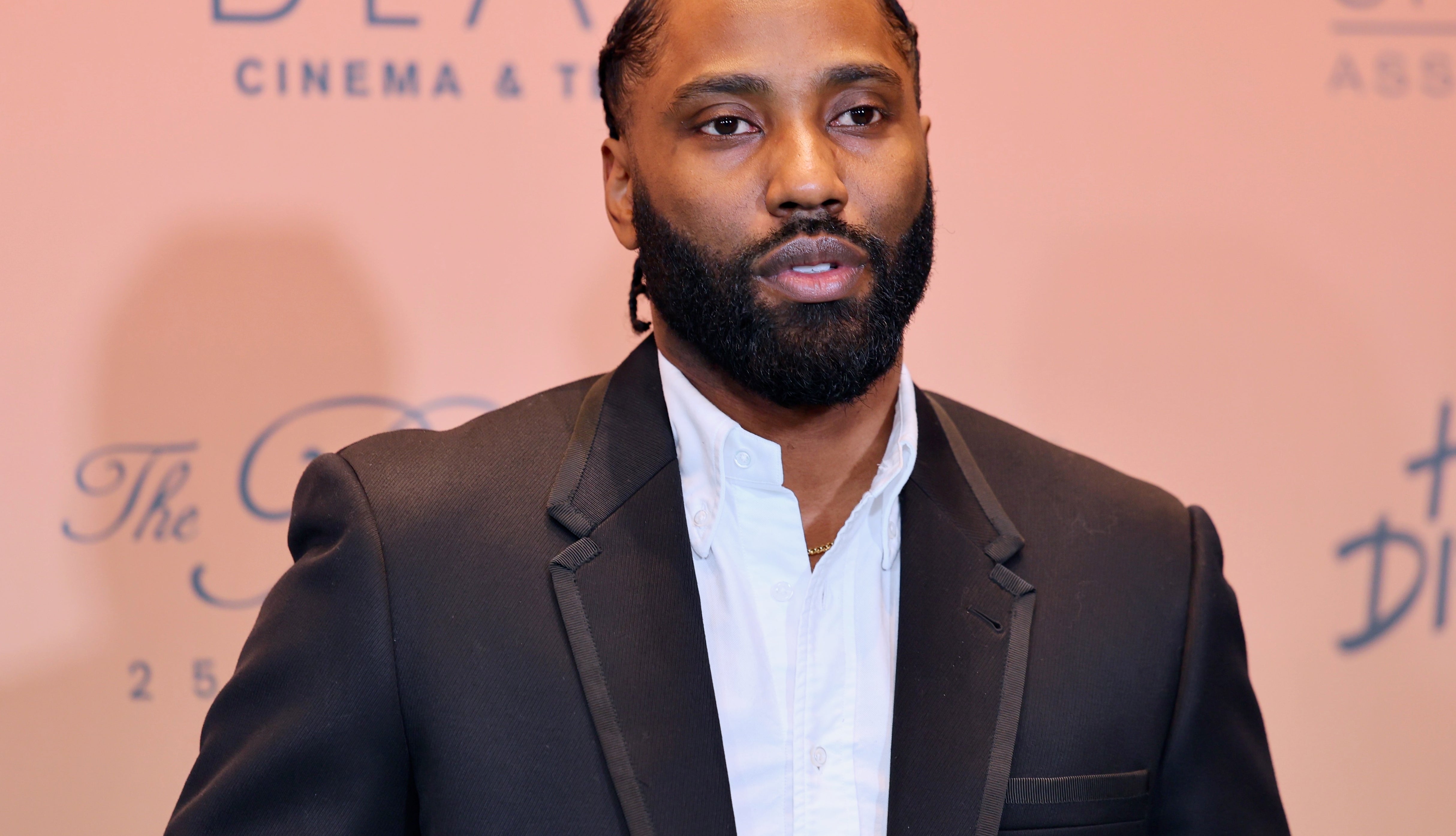 Person in a suit with a white shirt on a red carpet at a cinematic event backdrop