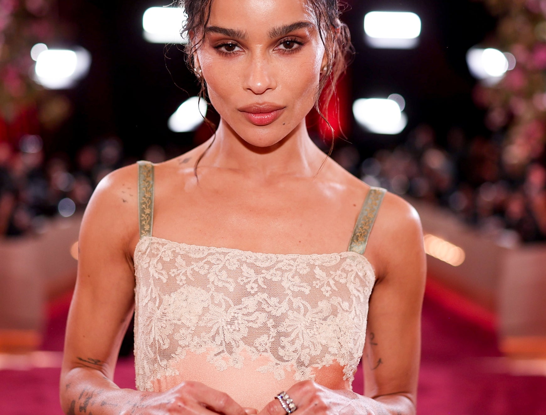 A person in an elegant evening gown poses on a red carpet, with photographers in the background capturing the moment