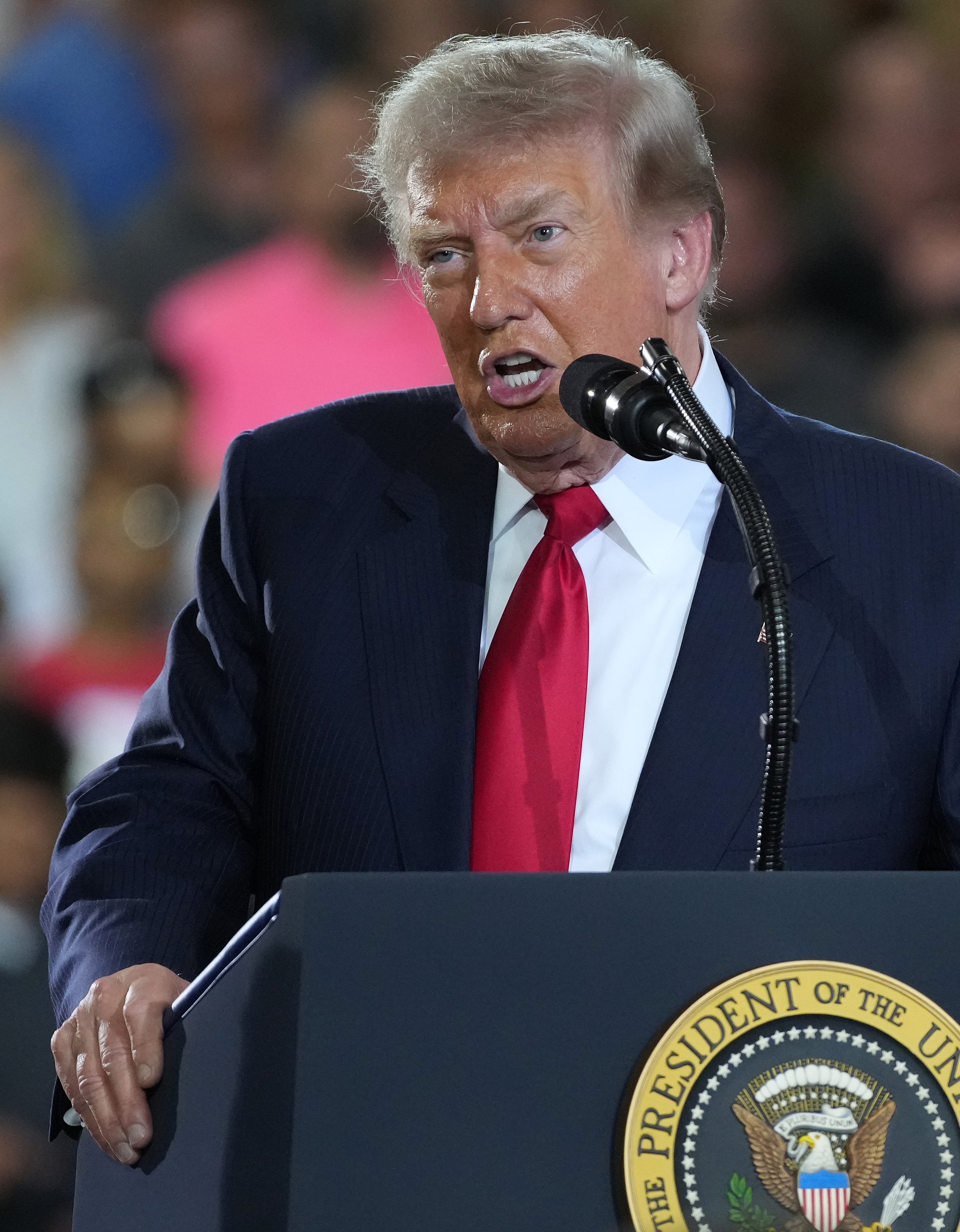 En person som snakker på et podium med presidentseglet, en annen person som applauderer ved siden av dem i en overfylt innendørs setting
