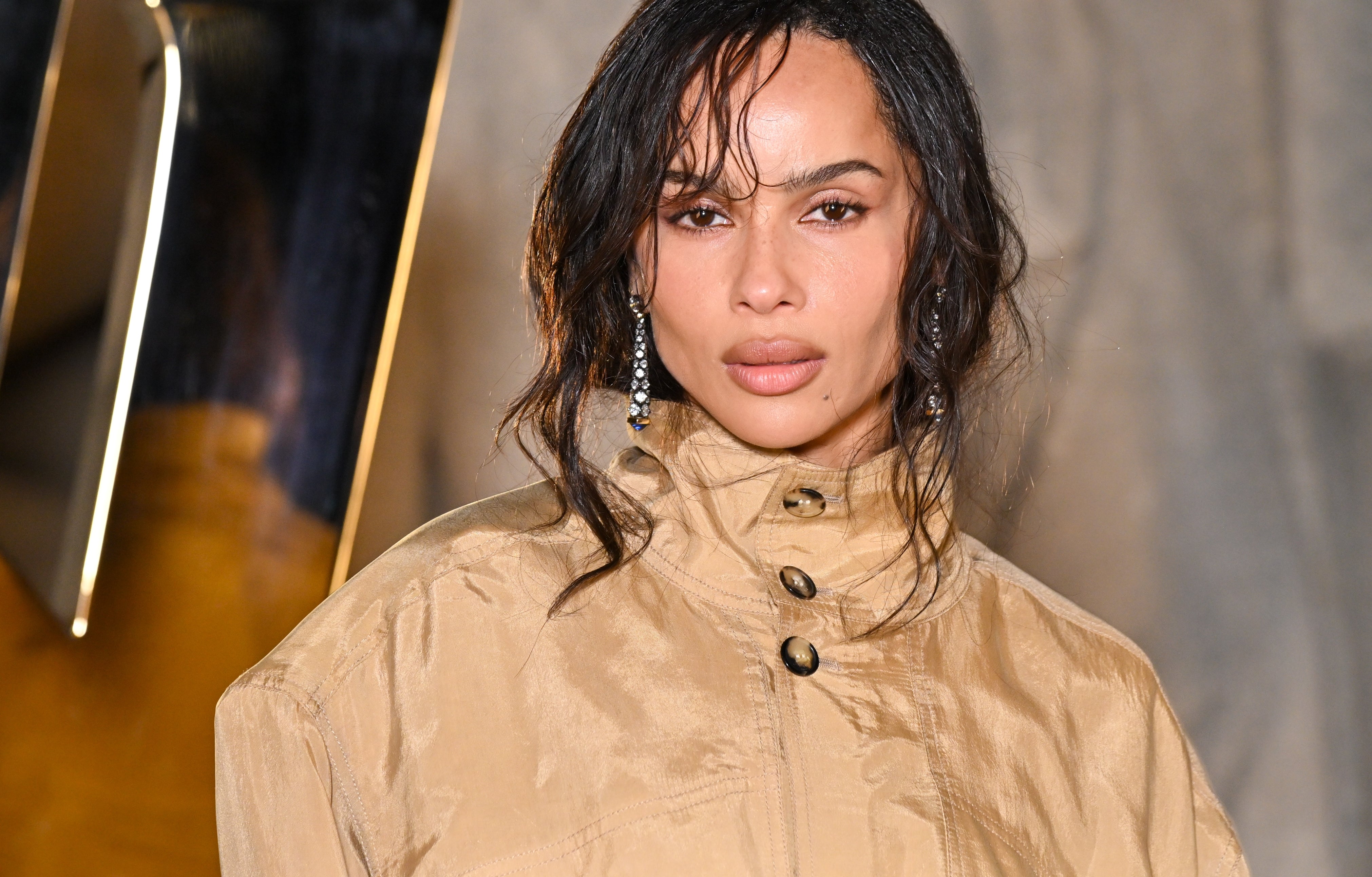 Person on a red carpet in a high-neck beige coat, styled with elegant earrings