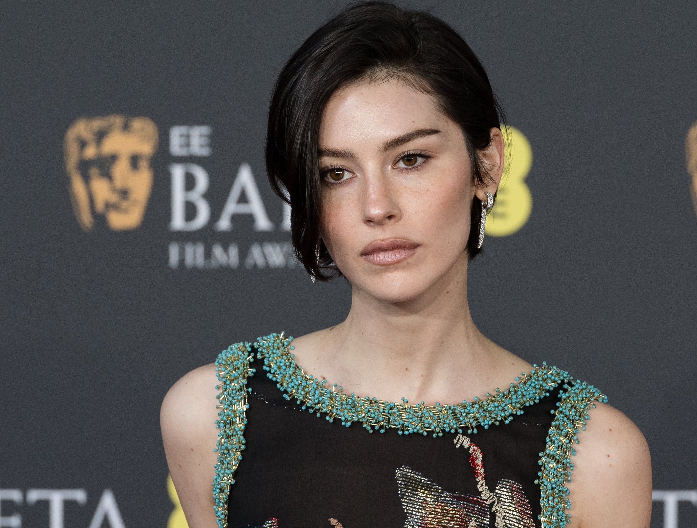 A person at the BAFTA Film Awards wearing a formal dress with intricate bead detailing, posing against a backdrop with event branding