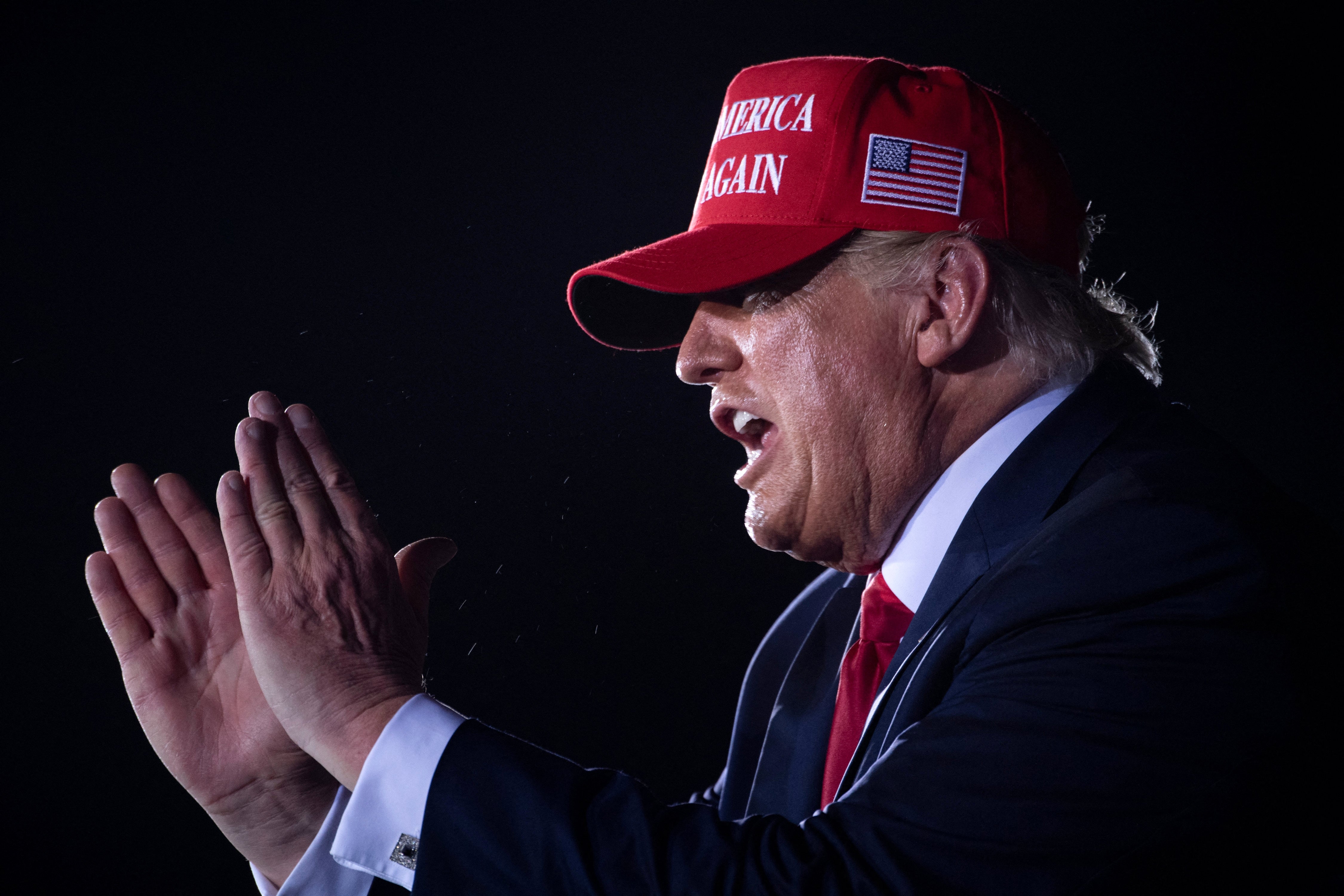Person som har på seg en "Make America Great Again" caps, klappende med et entusiastisk uttrykk, i mørk dress og rødt slips