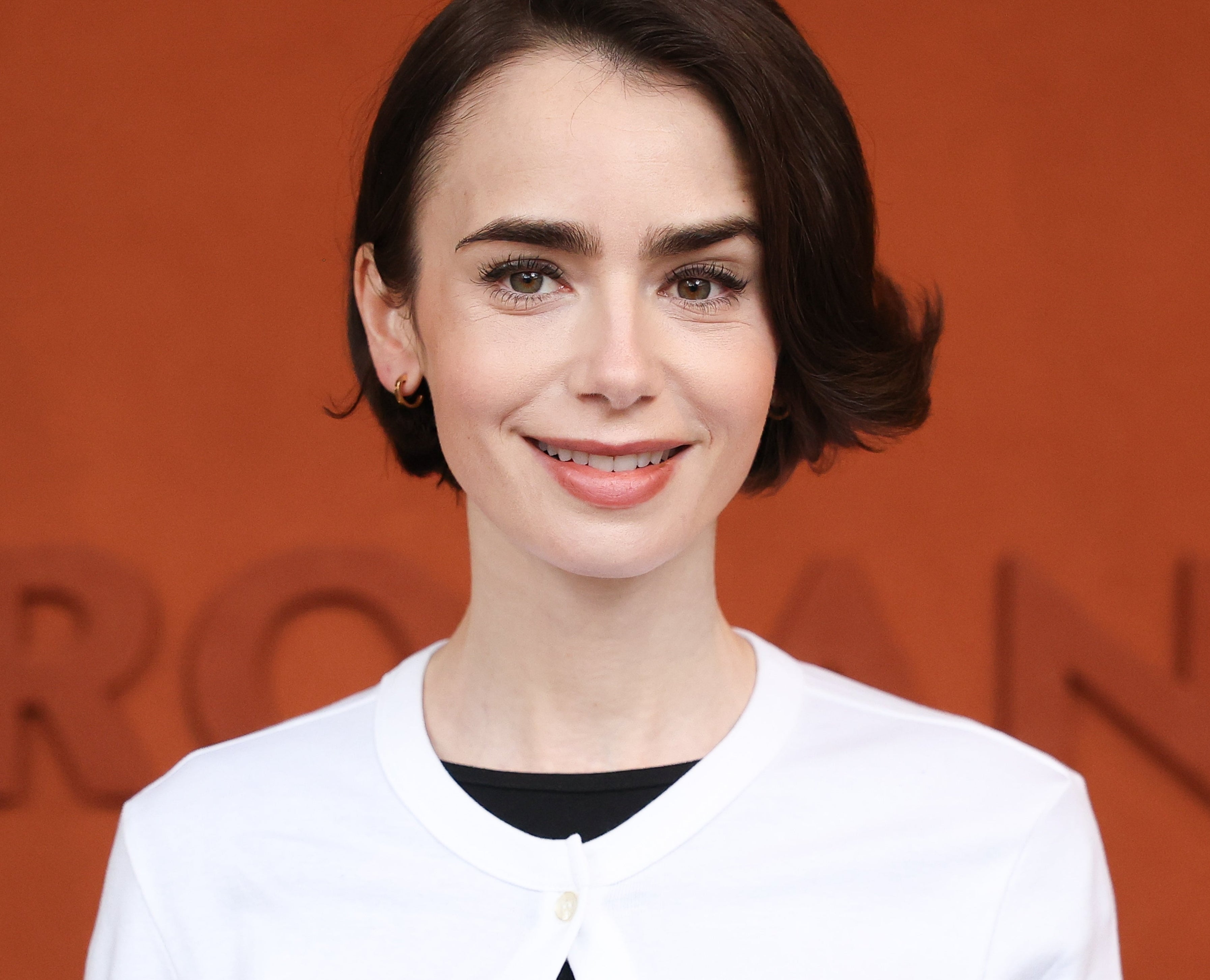 A person is smiling, wearing a simple and elegant white top with a black undershirt, at a formal event