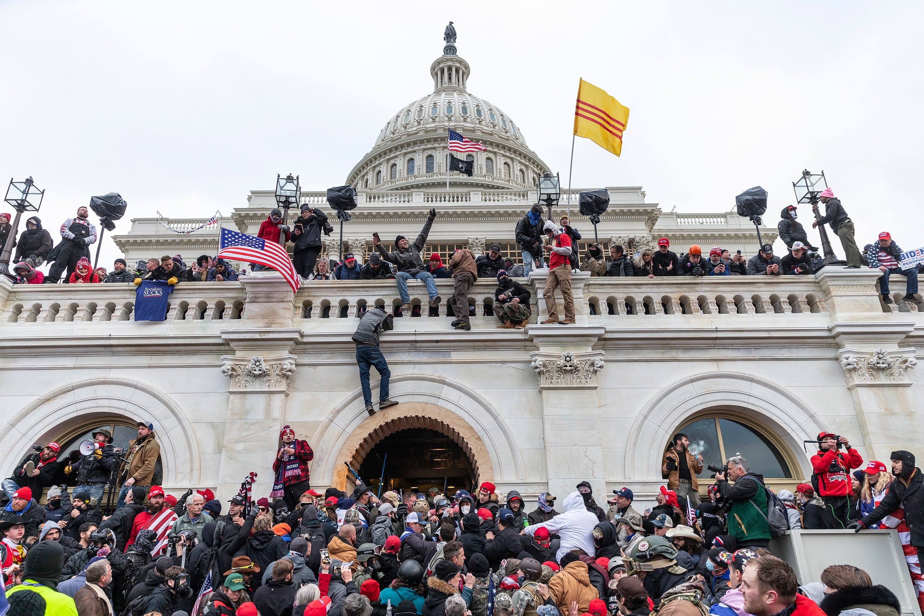 Folkemengder samles og klatrer på trappene og fasaden til den amerikanske Capitol-bygningen, med flagg, under en kaotisk offentlig begivenhet