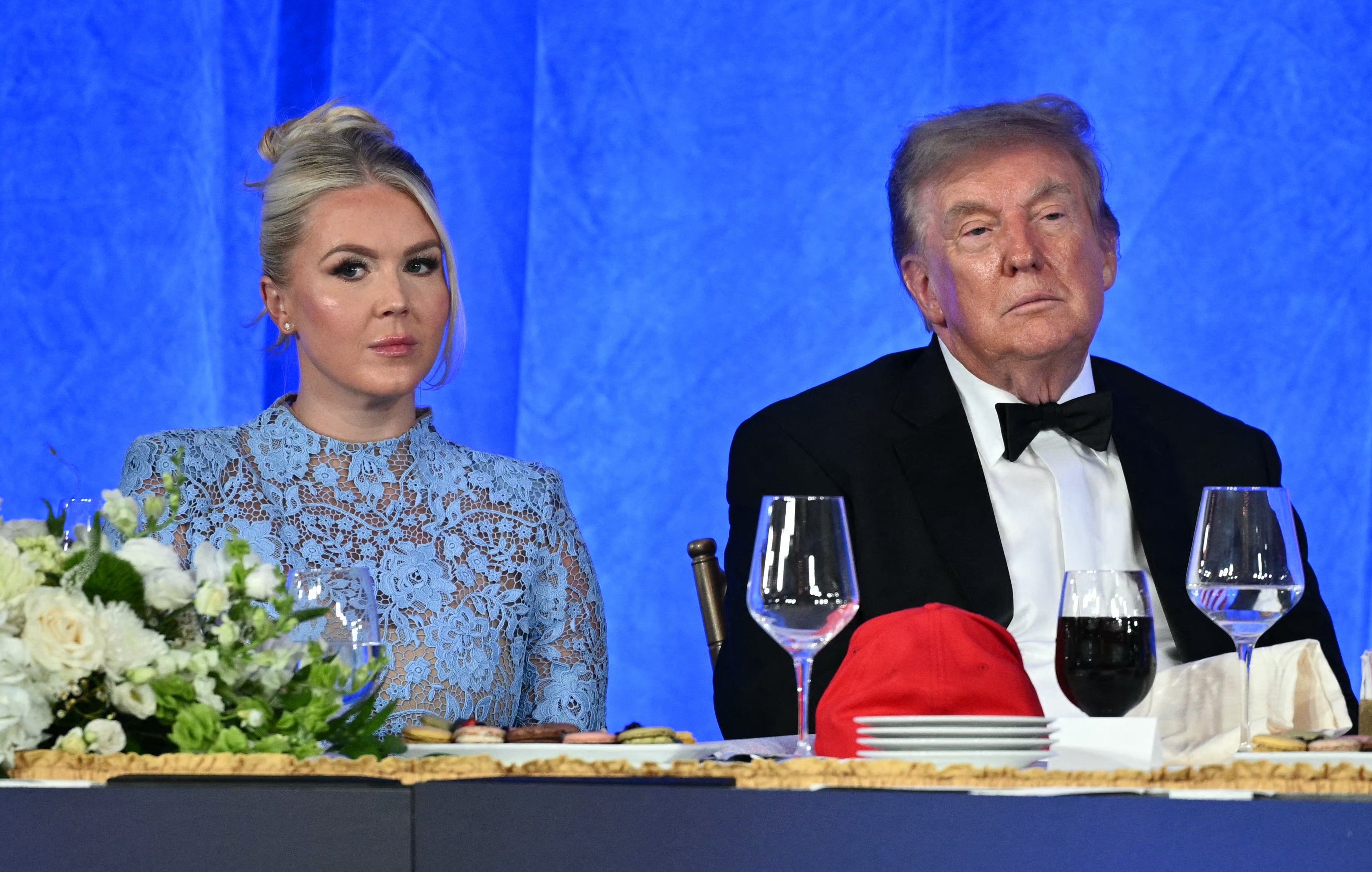 Et formelt arrangement med deltakere ved et bord. En kvinne i en elegant kjole og en mann i en smoking er til stede. Et amerikansk flagg er synlig