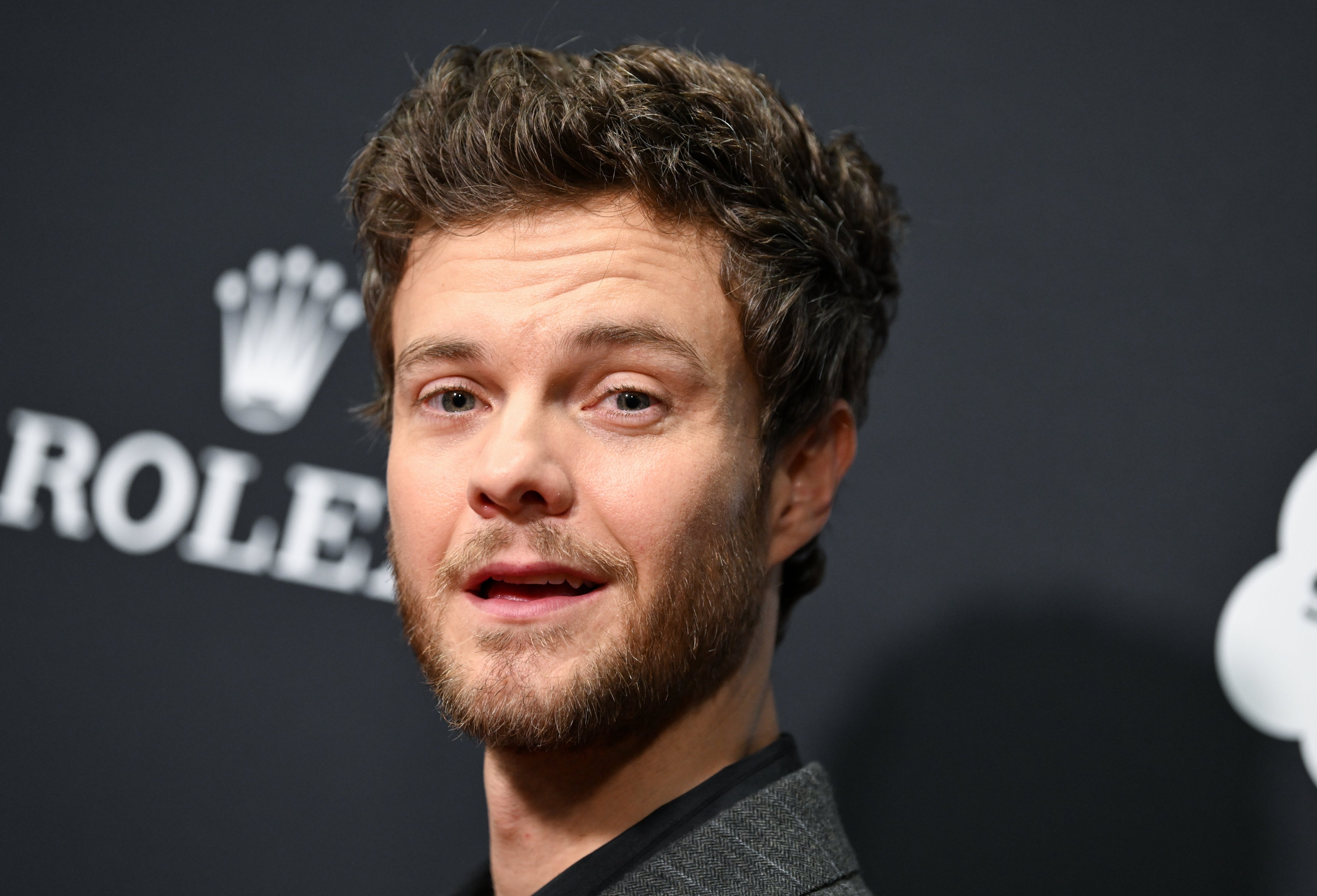 A man with a short beard and wavy hair attends an event, wearing a textured blazer
