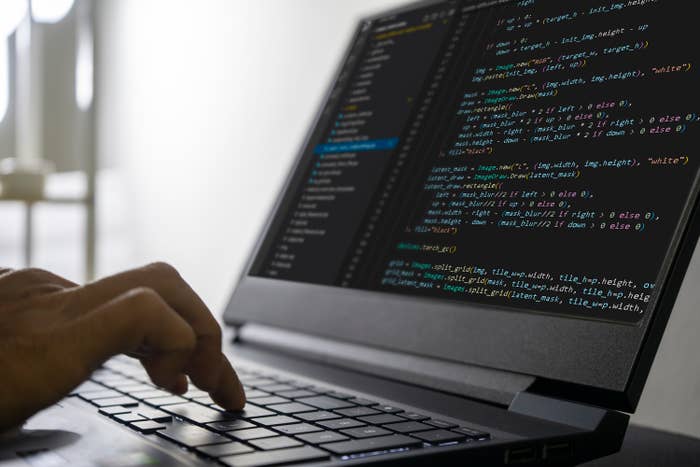 Person typing code on a laptop, screen shows lines of programming code