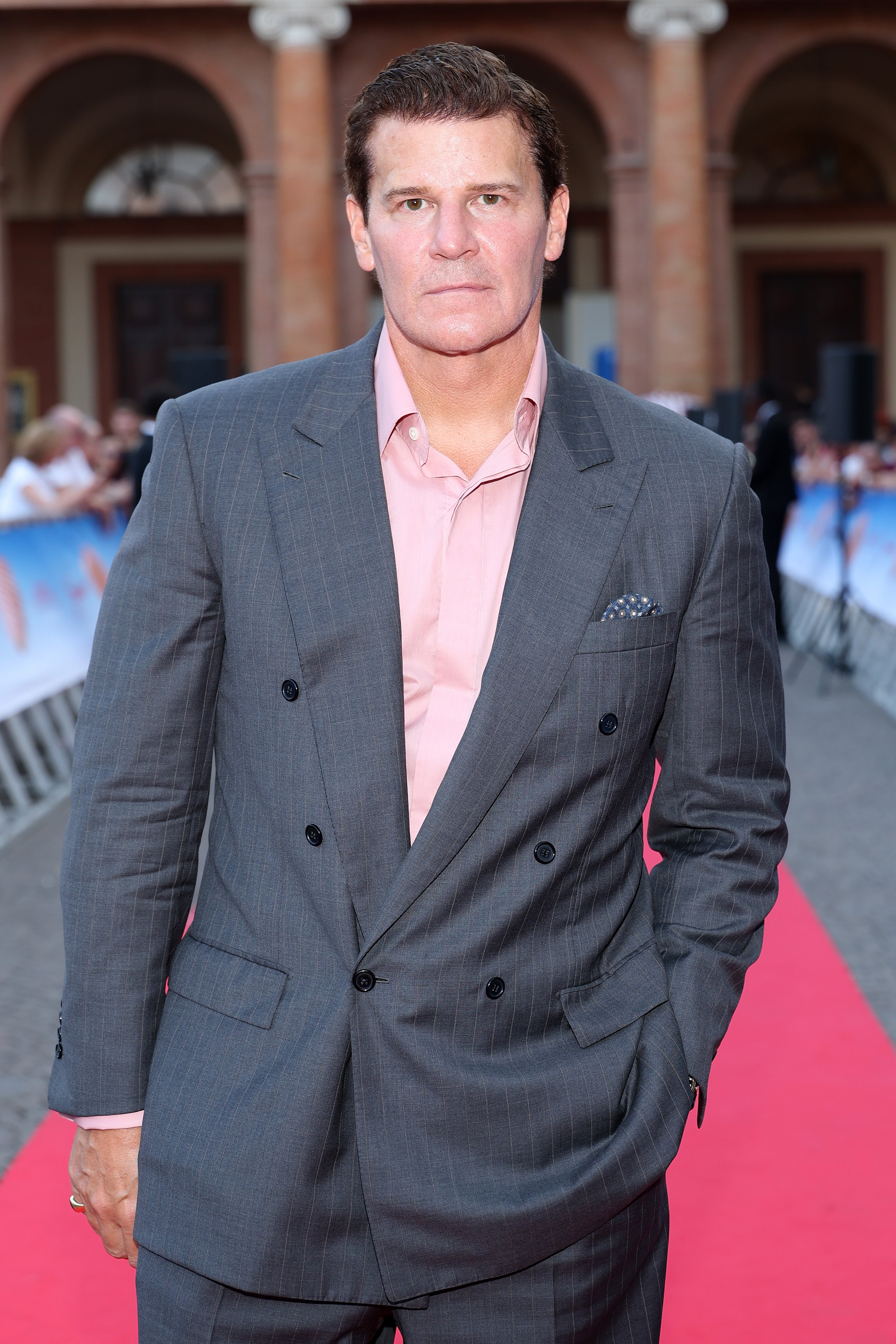 Person in a double-breasted suit and pink shirt on a red carpet, hand in pocket