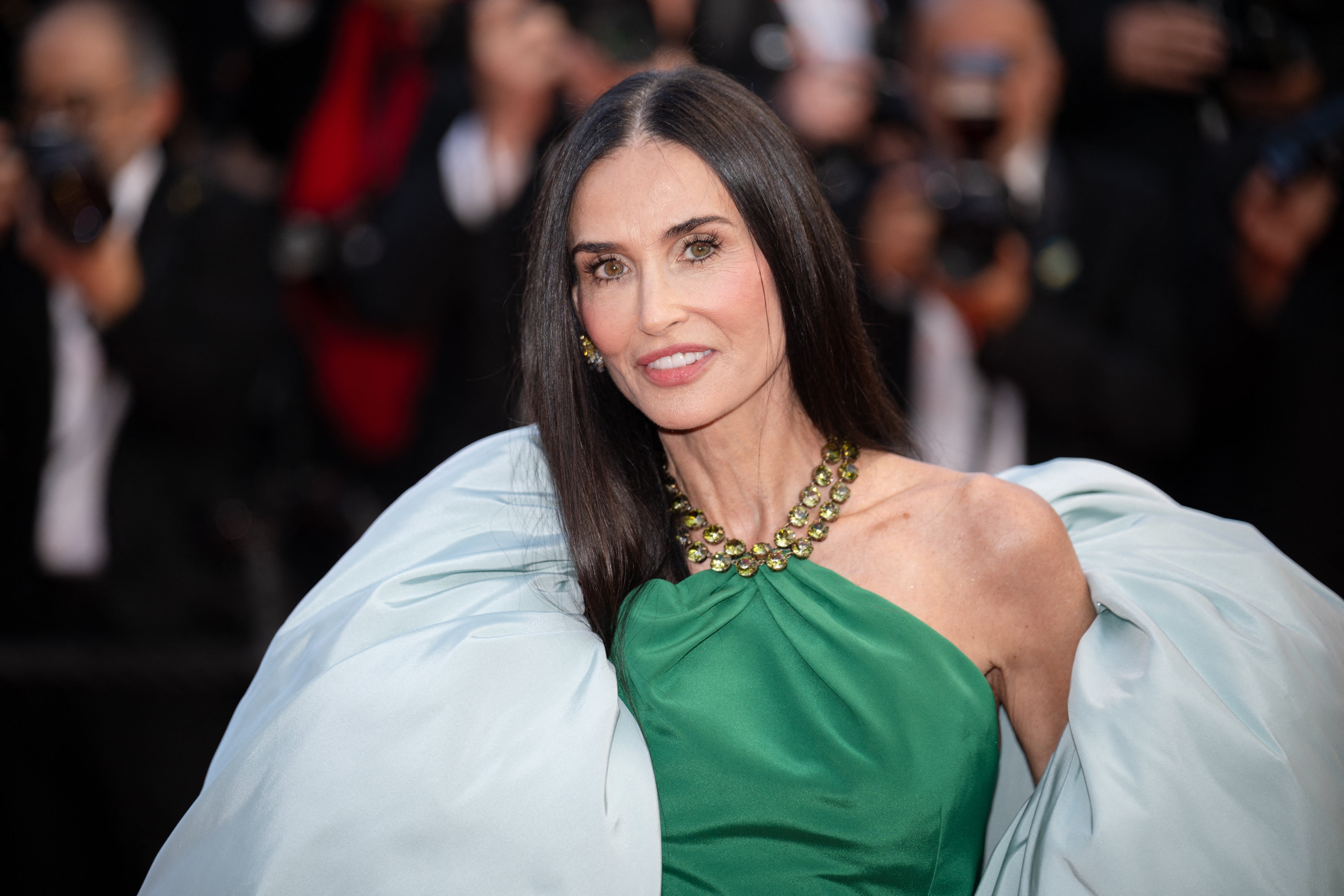 Person on red carpet in elegant green gown with a beaded neckline, posing for photographers