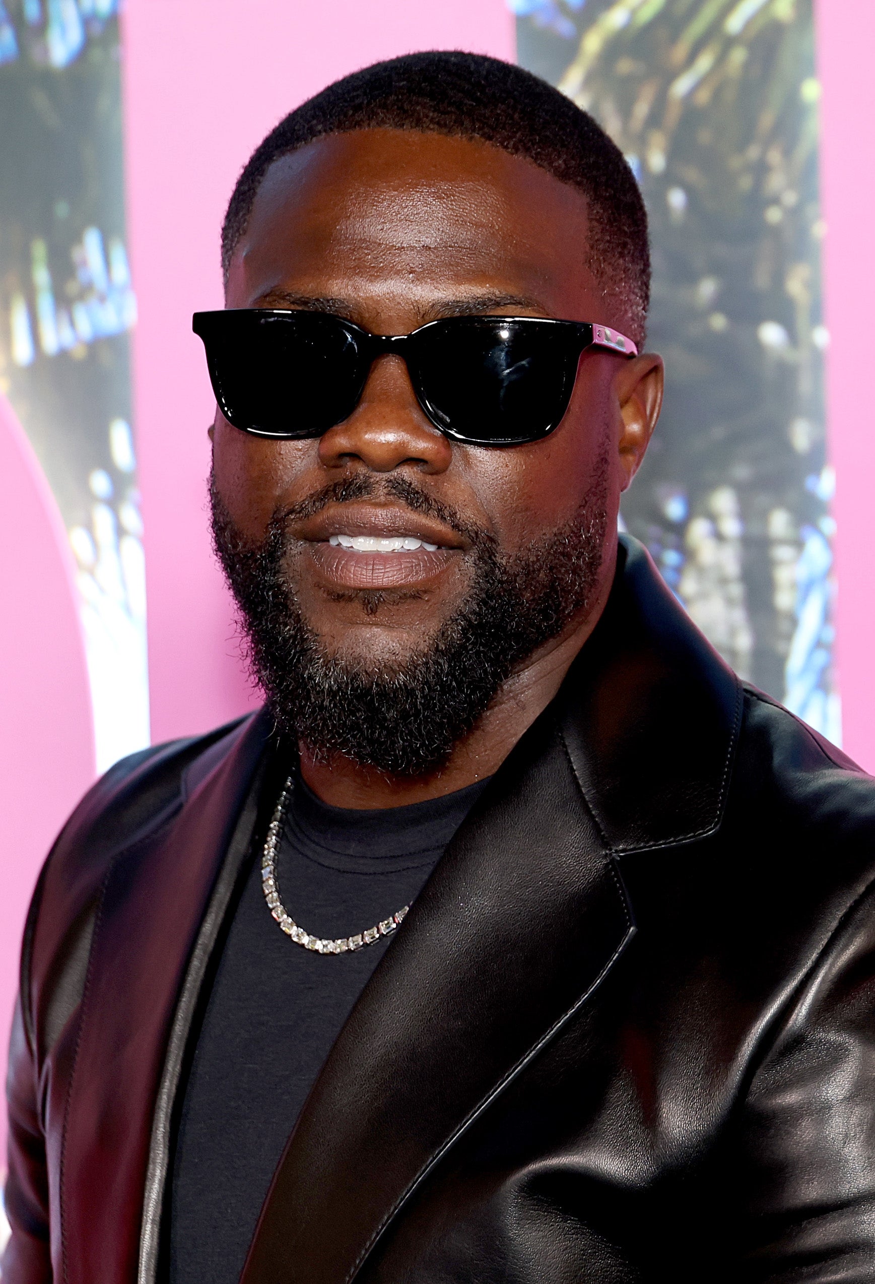 Man in sunglasses wearing a black leather jacket and chain necklace at a celebrity event