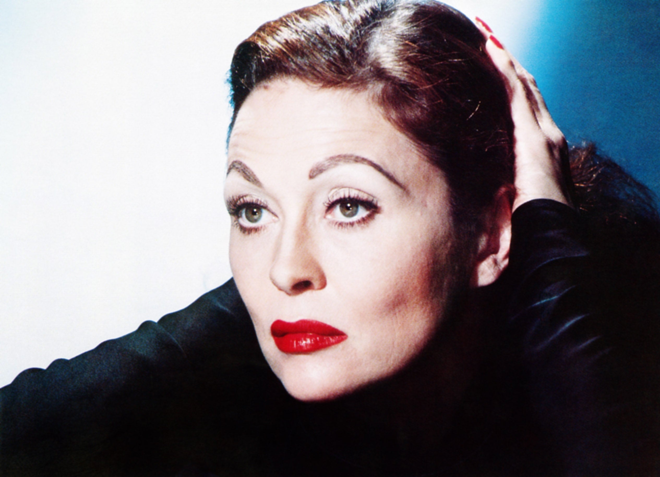 Faye Dunaway, with classic makeup and a sleek hairstyle, rests her hand on her head, gazing thoughtfully