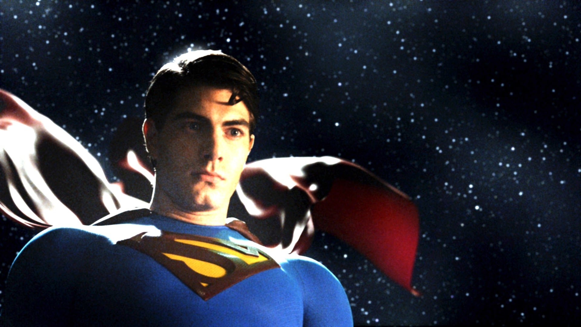 Brandon Routh in Superman costume stands against a starry sky backdrop, cape flowing behind him