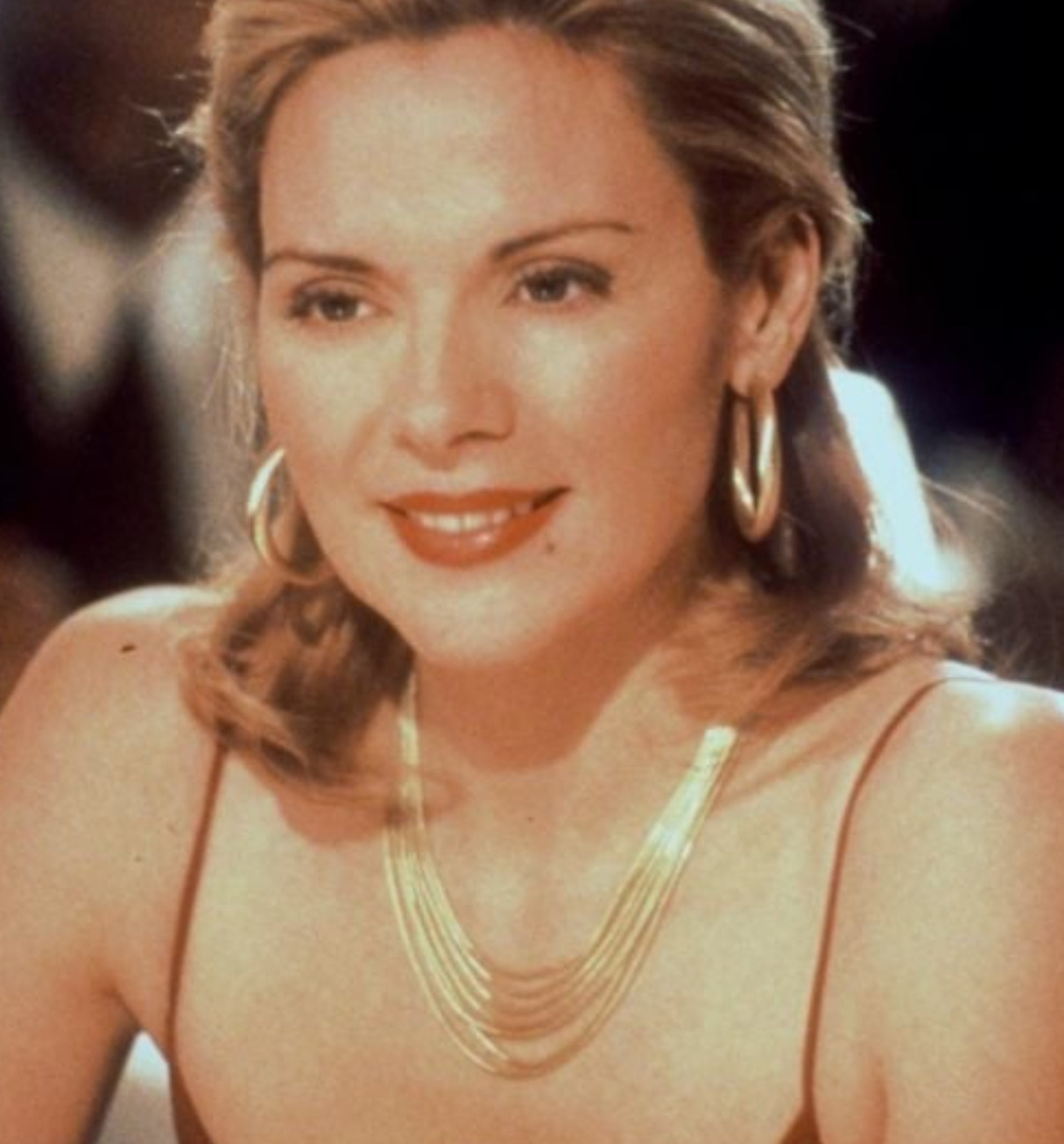 Person in a stylish outfit with hoop earrings and layered necklace, smiling at a table in a classy setting