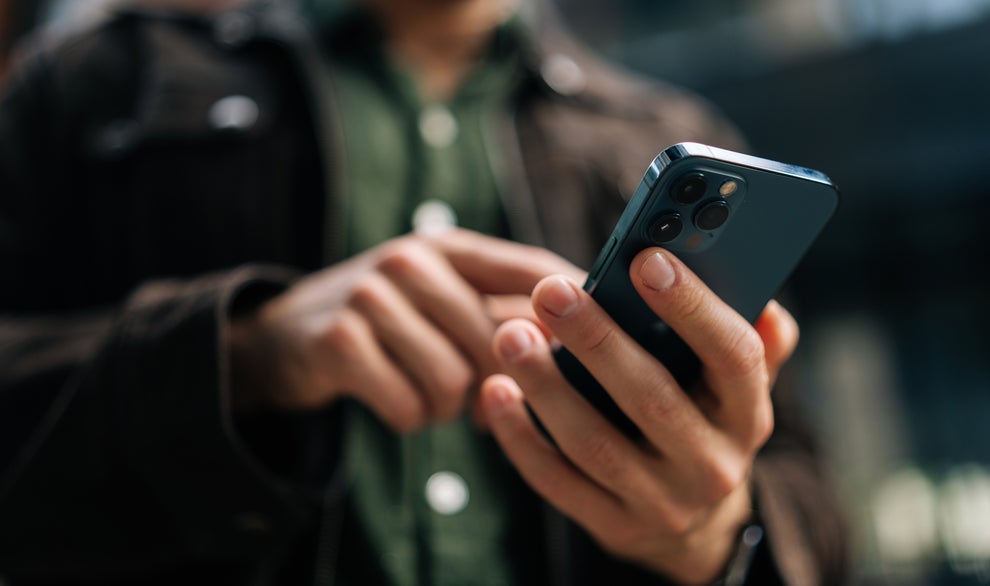 Person using a smartphone outdoors, focusing on the phone screen with their hands visible and body slightly blurred in the background