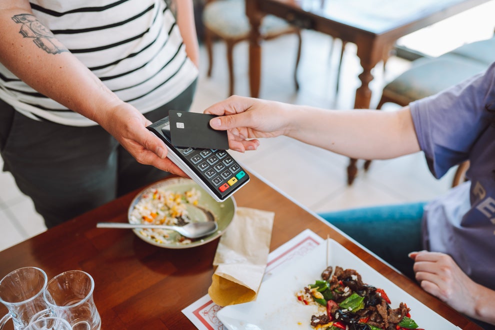 A person pays with a credit card using a card reader held by another person in a restaurant. Plates of food are on the table