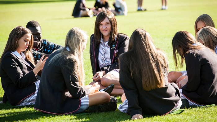 Group of students in school uniforms sitting on grass, some using phones, chatting, and relaxing