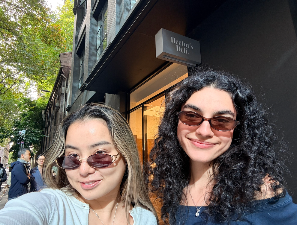 Two people wearing sunglasses smiling in front of Hector's Deli
