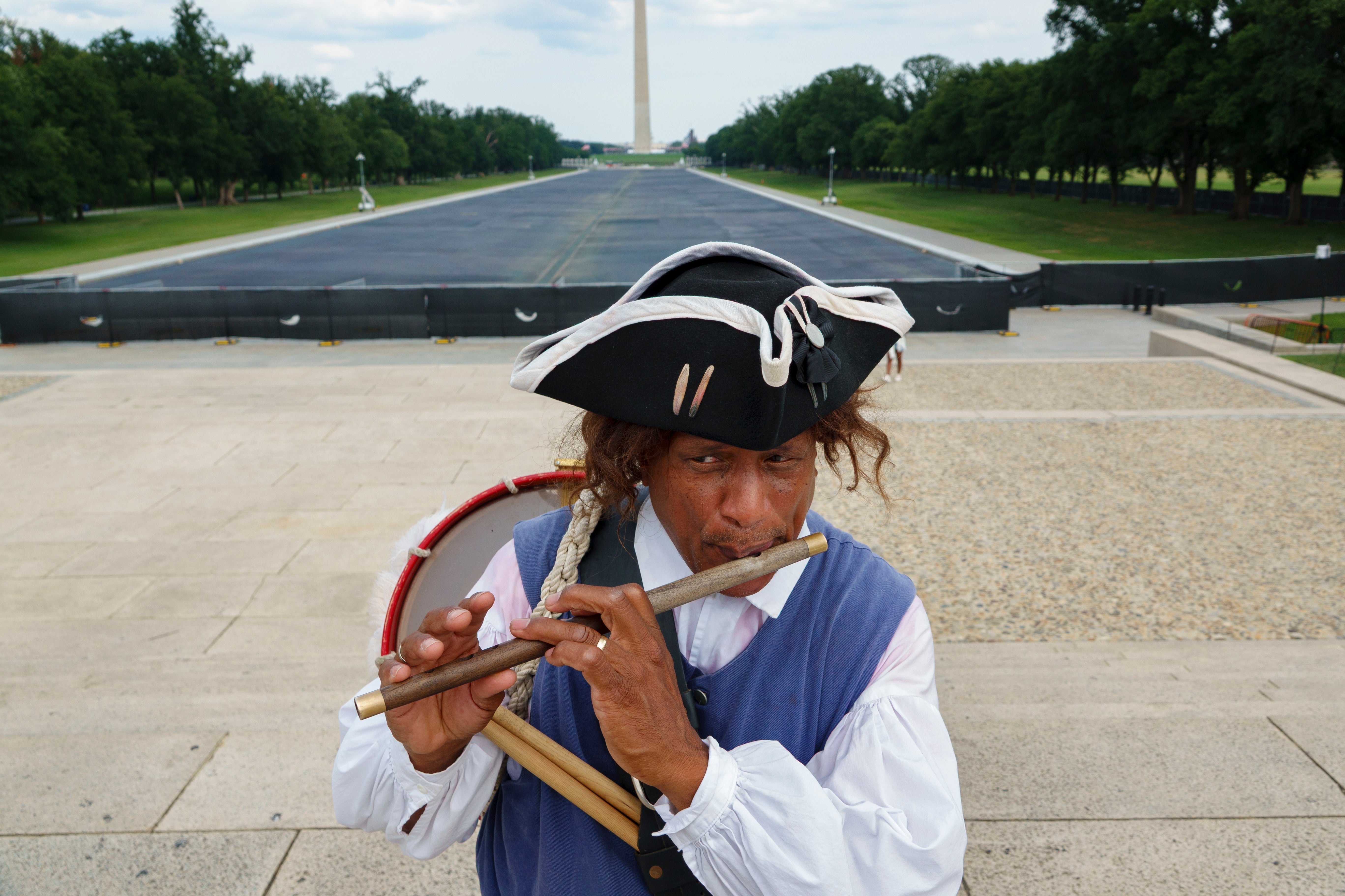 Person i 1700-tallsdrakt spiller på fløyte foran National Mall, med Washington-monumentet synlig i bakgrunnen