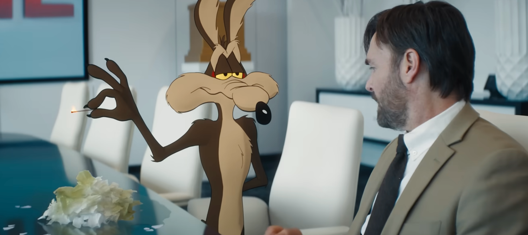 Coyote about to light something on fire on a desk, a man looks on in "Coyote vs. Acme"