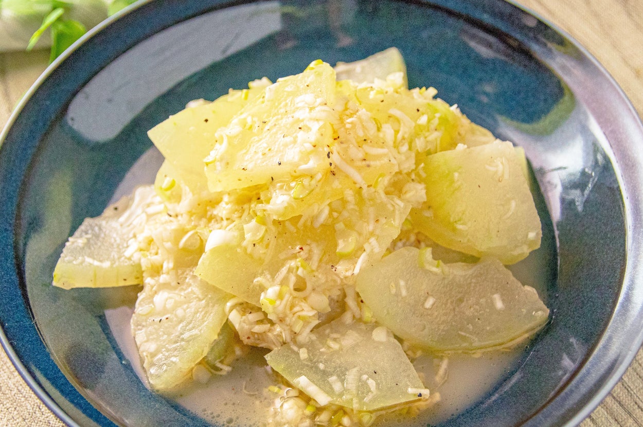 お皿に盛られたカットされた冬瓜と細かく刻まれた食材の料理。背景に緑の葉が見える。