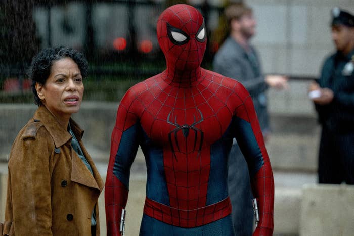 Spider-Man stands next to a concerned woman in a brown coat, both focused on something unseen