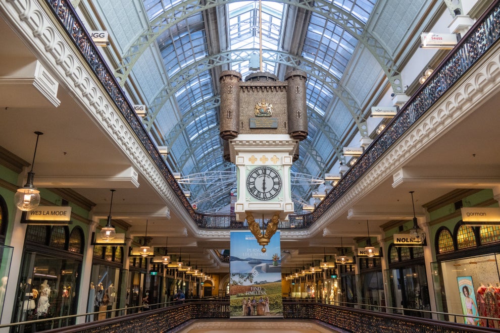 Clock inside a grand, ornate shopping arcade with high arched glass ceilings, showcasing an elegant blend of historic and modern architectural design