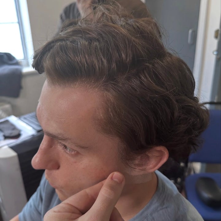 Person getting a facial prosthetic applied; fingers hold the edge of the prosthetic near their cheek