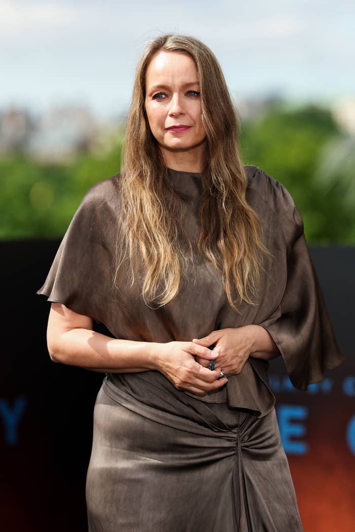 Person in elegant, draped dress poses outdoors at an event, standing with hands clasped
