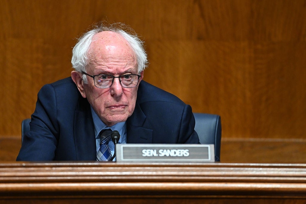 Bernie Sanders in glasses wearing a suit sits at a hearing, focused and attentive