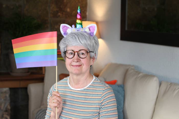 Person with unicorn headband holds pride flag, sitting on a couch