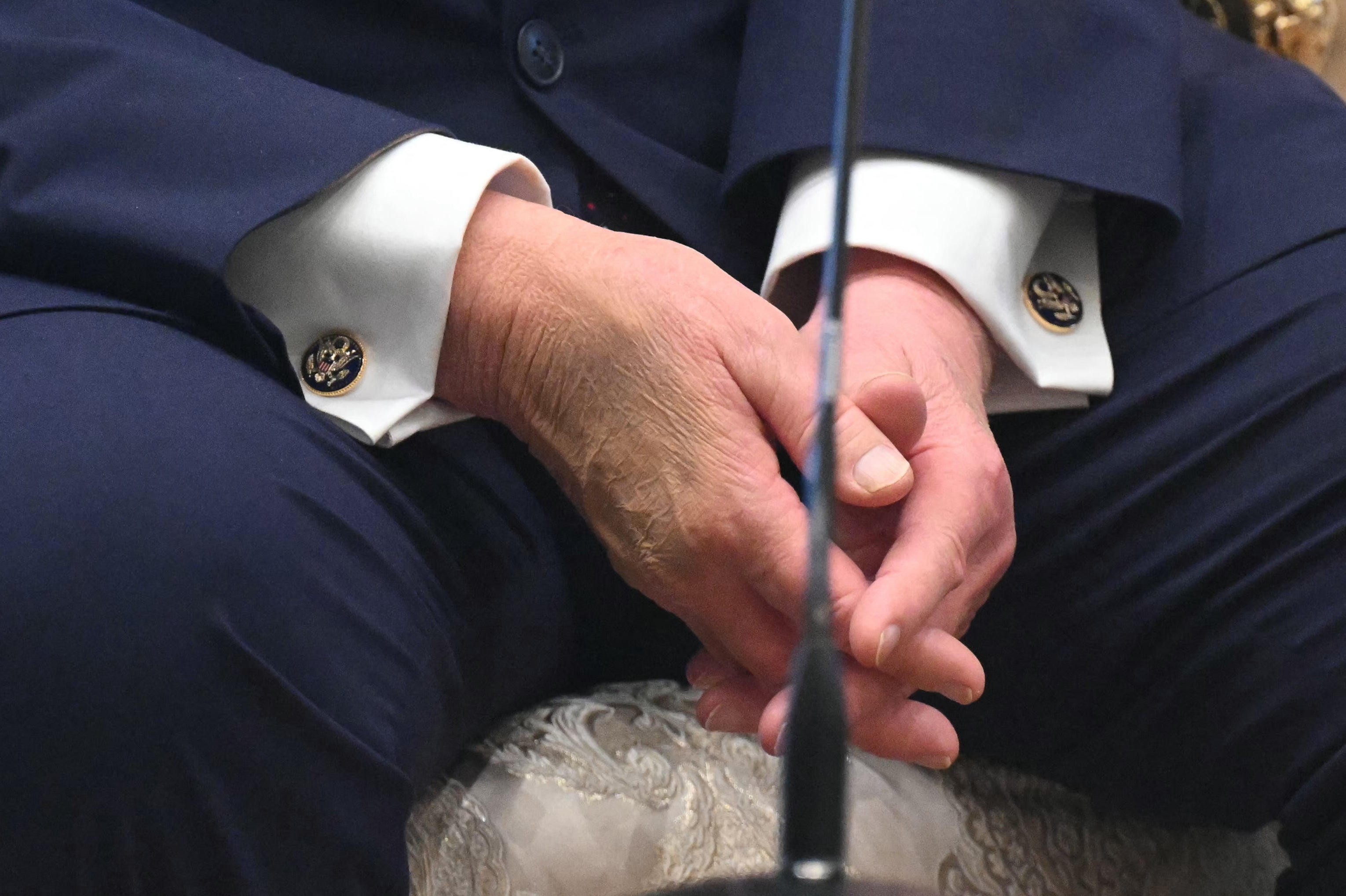 Person i en formell dress sittende med hendene sammen, og viser detaljerte mansjettknapper