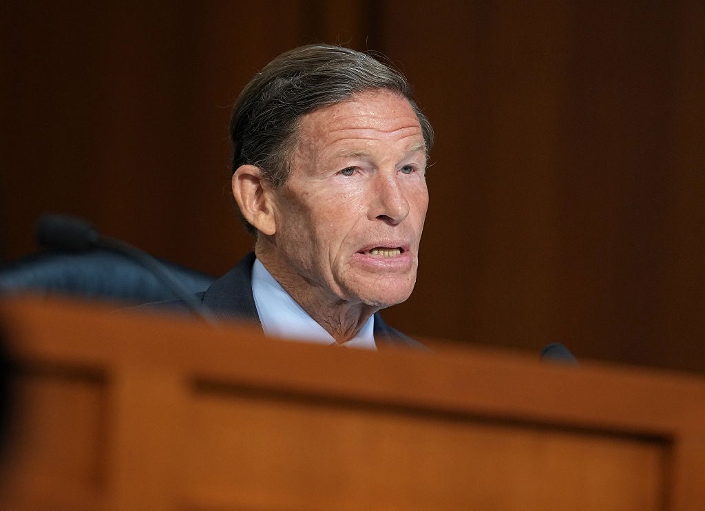 Richard Blumenthal speaking at a public hearing, wearing a suit and tie, seated behind a wooden panel