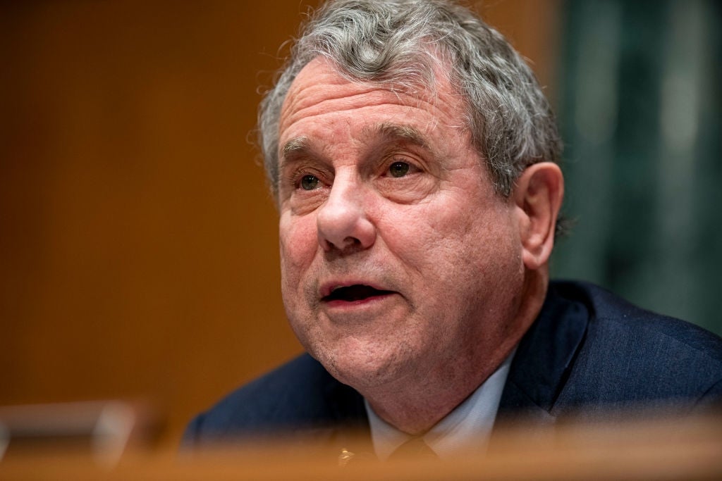 Sherrod Brown speaking at an indoor event, wearing a formal suit and looking engaged in conversation or discussion