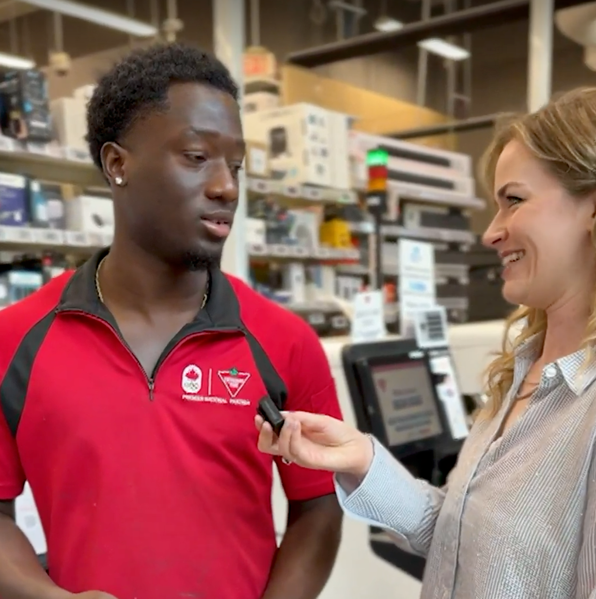 Two people in a store, one wearing a red work shirt, in conversation