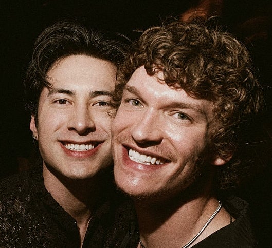 Three people smiling and posing closely together at an event. They are wearing stylish, dark clothing suitable for a night out