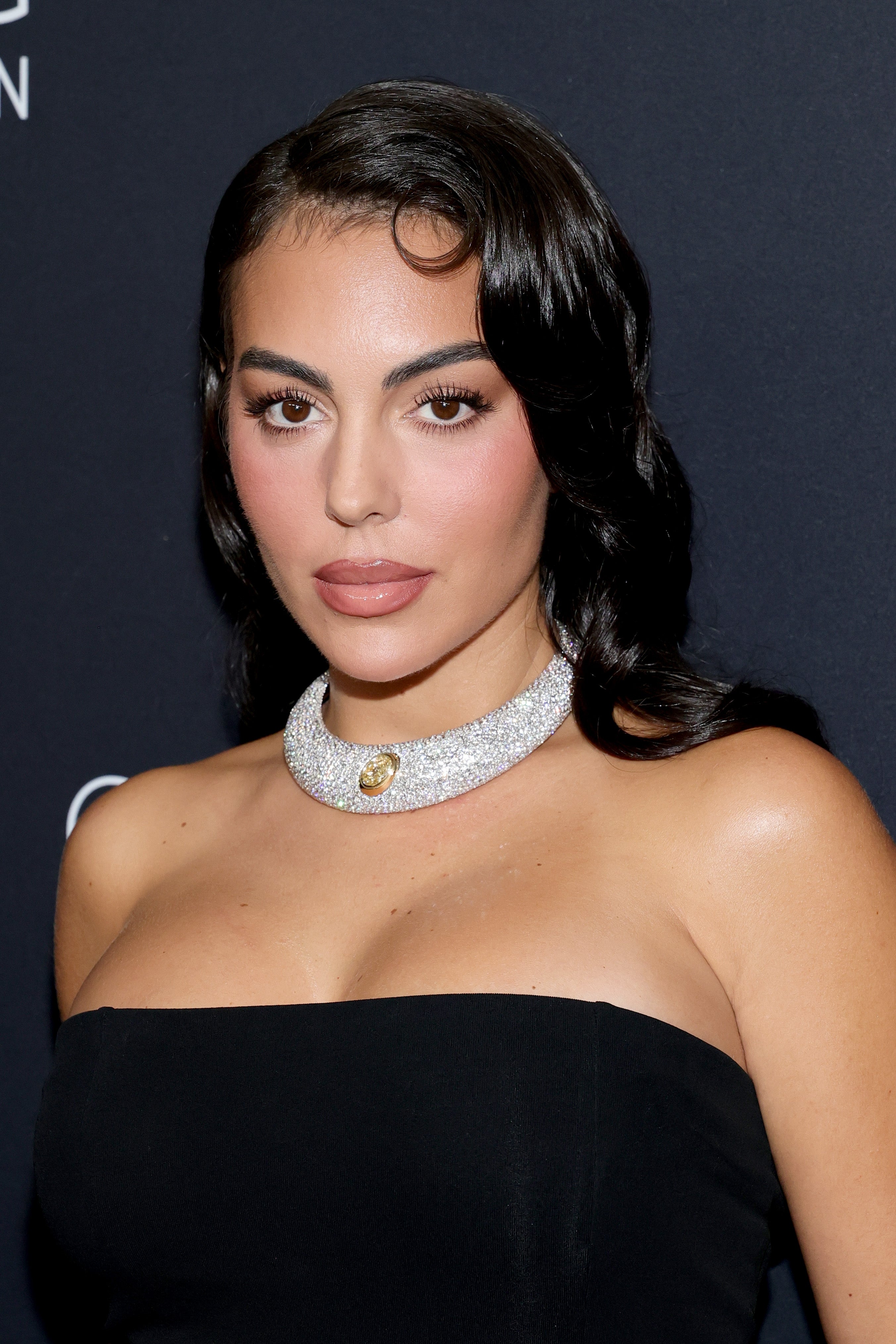 A person poses on the red carpet in an elegant off-shoulder gown with a sparkling choker necklace