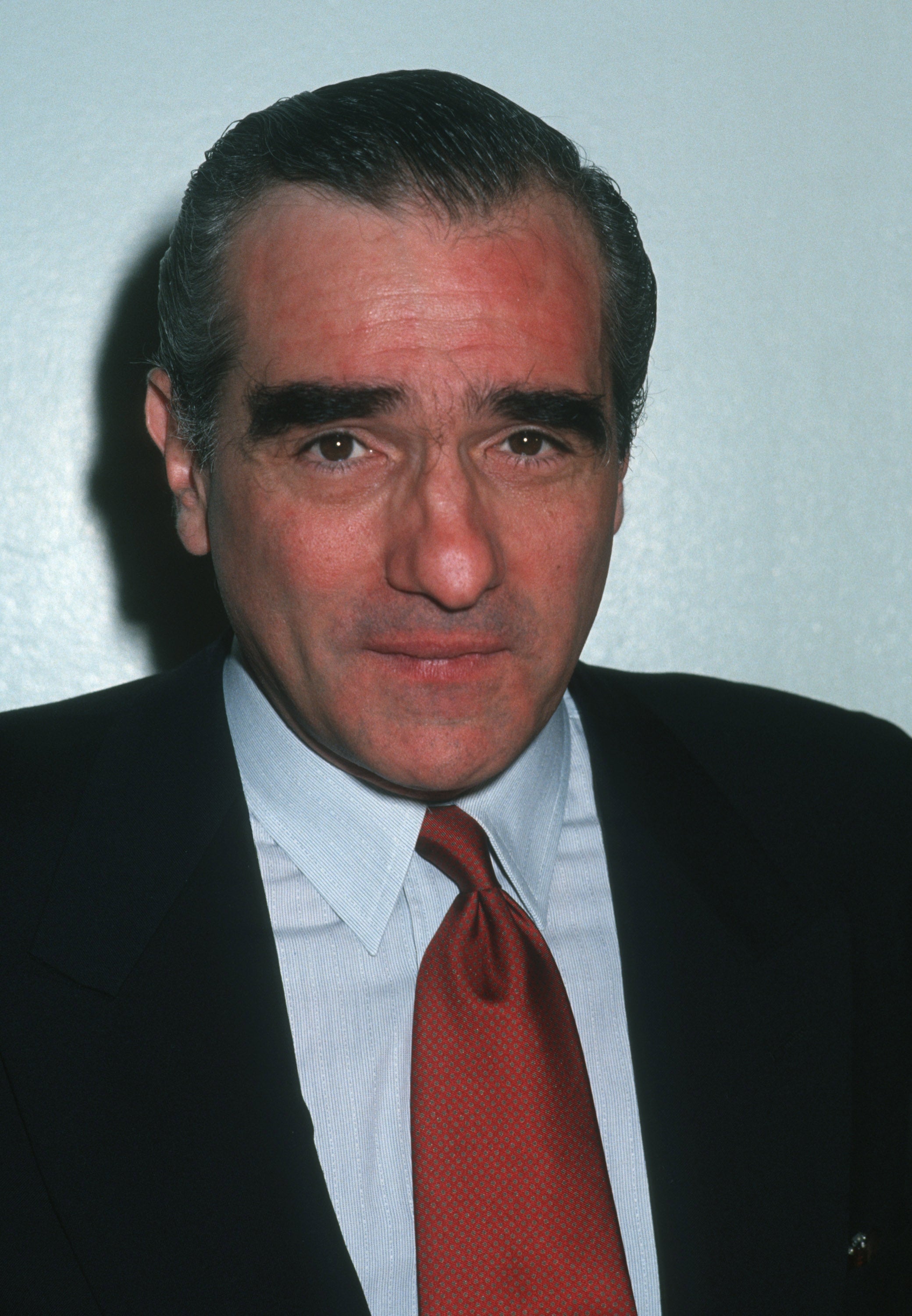 Person in a suit and tie with a slicked-back hairstyle, facing the camera