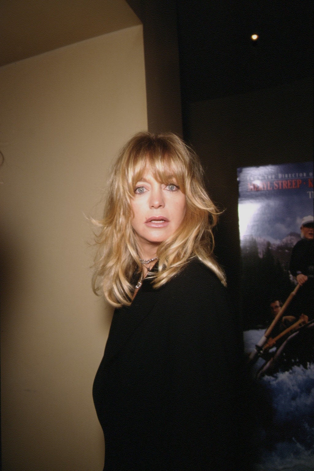 Person with long hair in a black outfit looks over their shoulder at an indoor event