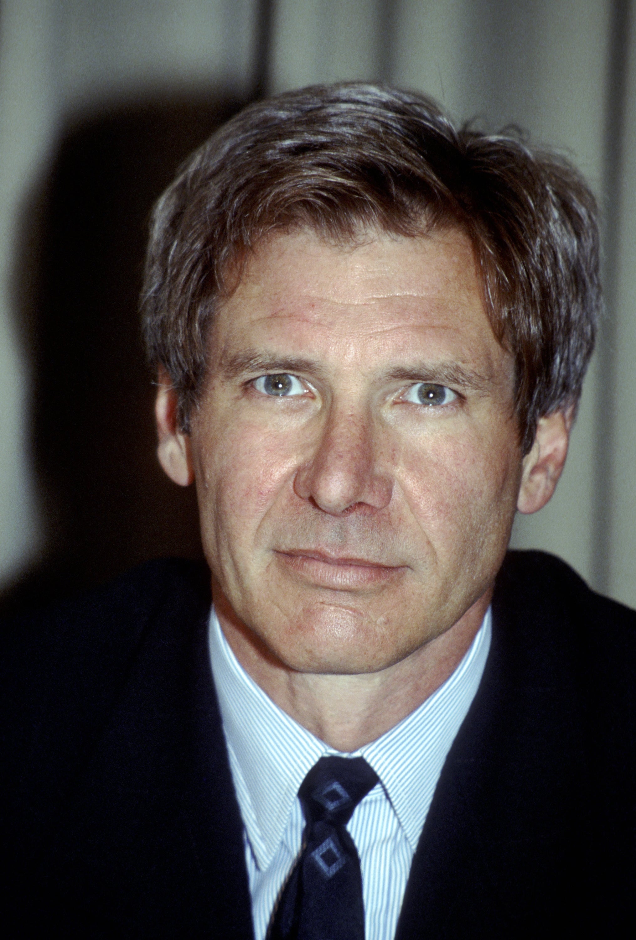 A person in a suit and tie, looking directly at the camera with a neutral expression