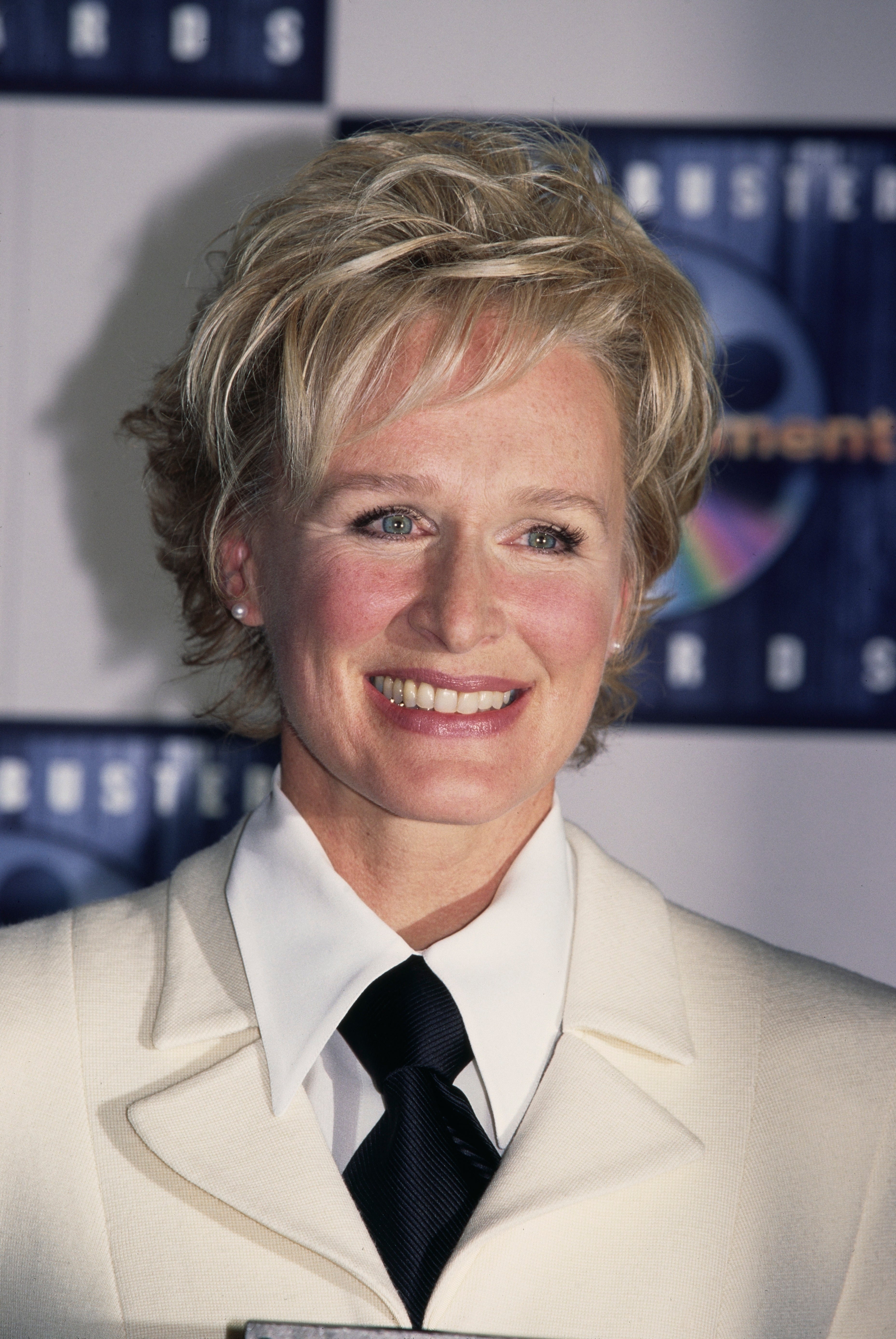 Person in a formal white suit with a black tie at an event, smiling at the camera